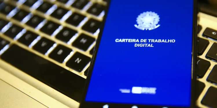 Smartphone com tela azul aberta no app Carteira de Trabalho Digital sobre teclado de notebook