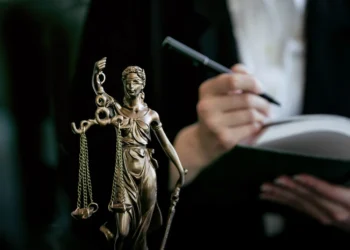 Estátua de Lady Justice com balança, enquanto advogado anota em livro, representando o universo jurídico.