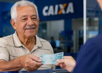 Idoso recebe uma nota de R$ 100 em uma agência bancária, representando os pagamentos de até R$ 8.475,55 do INSS referentes a julho.