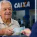 Idoso recebe uma nota de R$ 100 em uma agência bancária, representando os pagamentos de até R$ 8.475,55 do INSS referentes a julho.