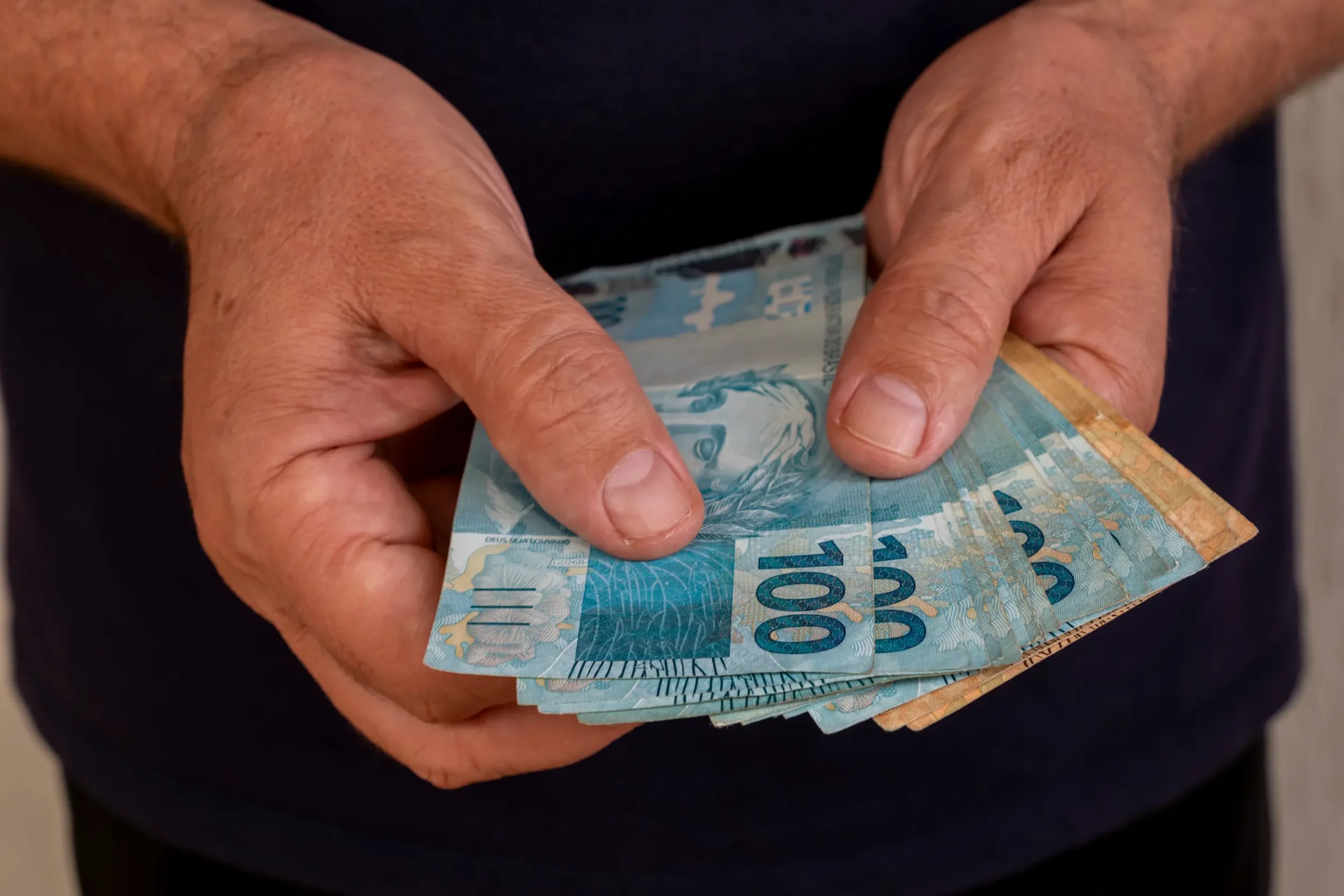 Pagamento de R$ 8.475,55 do INSS Pessoa segurando cédulas de R$ 100, ilustrando o pagamento do INSS no valor de R$ 8.475,55.