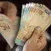 Notas de real sendo contadas à mão representando pagamento judicial liberado para segurados do INSS