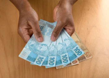 Pessoa segurando notas de cem e cinquenta reais simbolizando o pagamento do Pé-de-Meia.