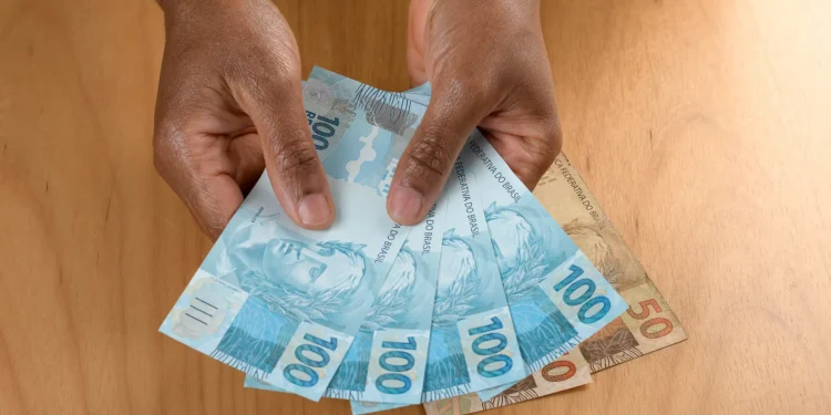 Pessoa segurando notas de cem e cinquenta reais simbolizando o pagamento do Pé-de-Meia.