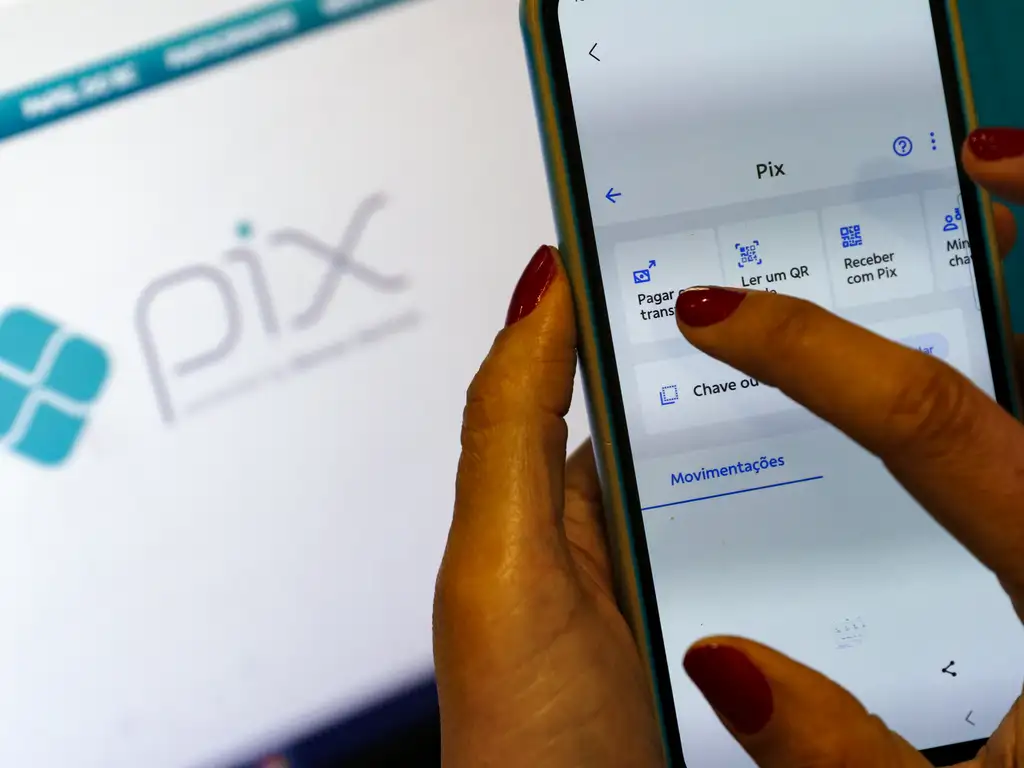 Pagamentos Pix Mão feminina utiliza smartphone para acessar opções de pagamento Pix com tela do serviço ao fundo