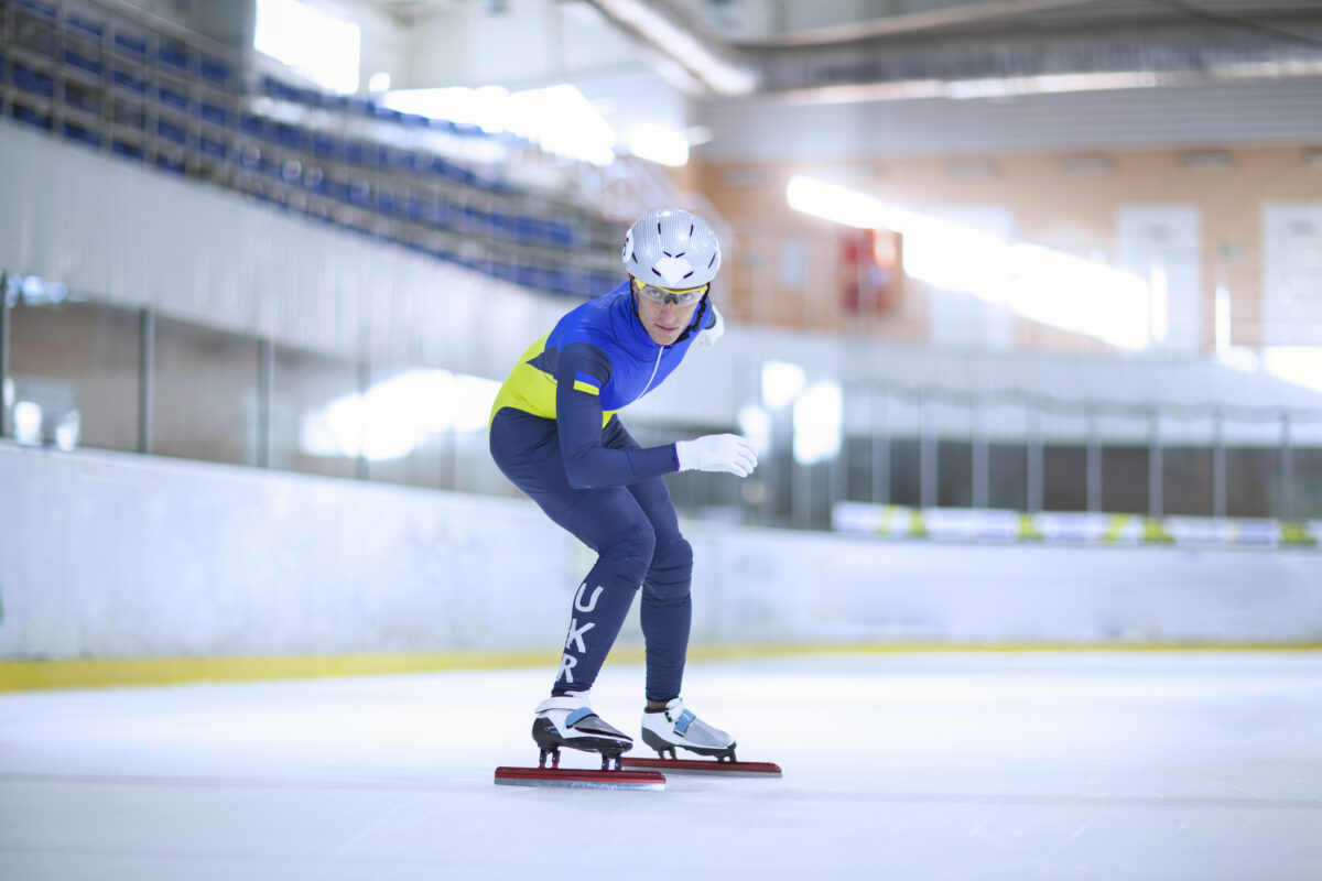 atinação de velocidade em pista curta nos Jogos Olímpicos de Inverno 2026. Atleta competindo na patinação de velocidade em pista curta, com foco em desempenho e técnica em um ambiente de gelo.