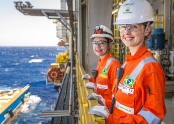 Duas funcionárias da Petrobras usando uniforme laranja e capacete em plataforma de petróleo no mar