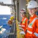 Duas funcionárias da Petrobras usando uniforme laranja e capacete em plataforma de petróleo no mar