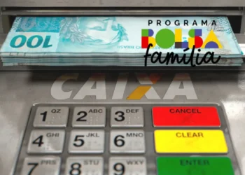 Cédulas de R$100 sendo retiradas de caixa eletrônico com painel do Bolsa Família e teclado numérico