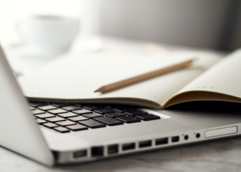 Caderno aberto com lápis repousa sobre teclado de notebook em mesa clara