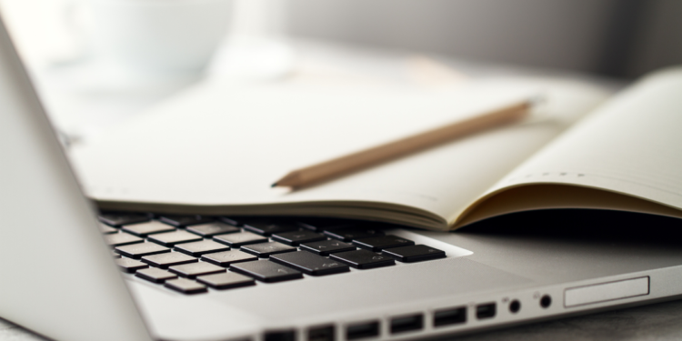 Caderno aberto com lápis repousa sobre teclado de notebook em mesa clara