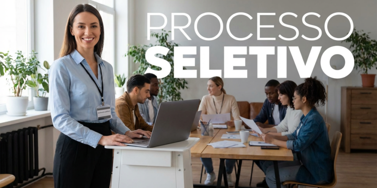 Mulher sorridente em pé ao lado de notebook liderando processo seletivo com equipe reunida ao fundo