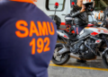 Socorrista do SAMU coloca capacete ao lado de moto de atendimento em base operacional
