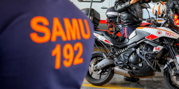 Socorrista do SAMU coloca capacete ao lado de moto de atendimento em base operacional