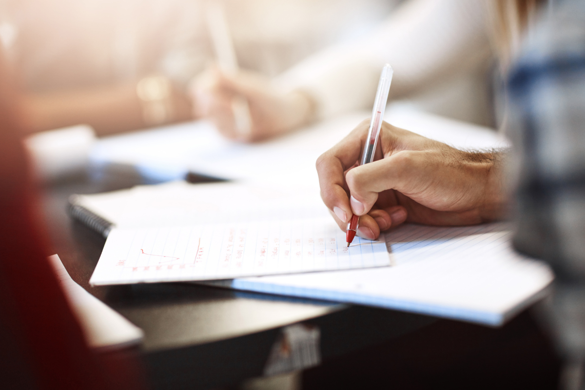 Processos Seletivos 2026 Pessoa segurando caneta vermelha anotando respostas em caderno durante exame