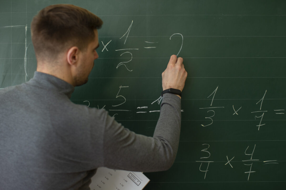 Curso de Matemática permite atuação com menos contato social Professor de matemática resolvendo cálculos e frações em quadro verde durante atividade de ensino ou pesquisa.