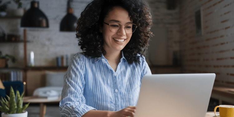 Mulher de óculos usando notebook e sorrindo em ambiente doméstico iluminado