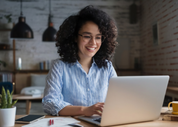 Pessoa sorrindo enquanto trabalha no computador, representando a busca por qualidade de vida no trabalho.