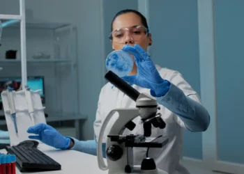 Profissional de saúde analisando uma amostra em laboratório com um microscópio, refletindo as oportunidades na área da saúde em 2026.