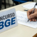 Candidato preenche cartão de respostas ao lado de placa com inscrição concurso IBGE