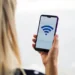 Mulher segurando smartphone com símbolo de Wi-Fi na tela, representando riscos de manter a conexão ativa o tempo todo.
