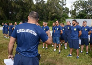 Instrutor orienta grupo de candidatos uniformizados alinhados em gramado durante TAF da Guarda Municipal 2026