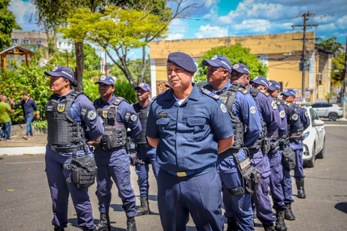 Vagas Guarda Municipal 2026 Guardas municipais uniformizados perfilados em rua, com árvores e prédios ao fundo.