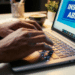 Pessoa digitando no teclado de notebook exibindo tela com mensagem inscrições abertas