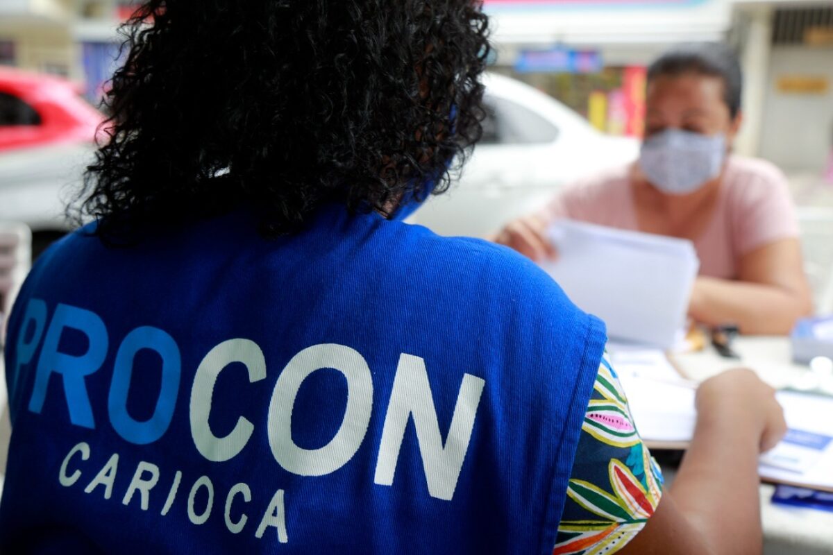 Vagas Procon RJ Funcionária do Procon Carioca conversa com mulher usando máscara e segurando papéis