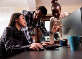 Estudantes de Ciência da Computação em laboratório de informática, com professor orientando análise de código e desenvolvimento de software.