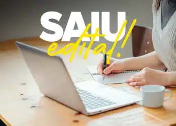 Mulher fazendo anotações e notebook aberto em cima da mesa.