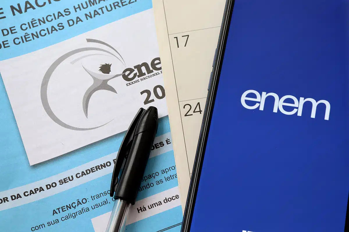 Caderno do Enem com caneta preta ao lado e celular exibindo logotipo do Enem sobre calendário, representando estudo para a prova após alterações no decreto presidencial que ampliou funções do Enem.