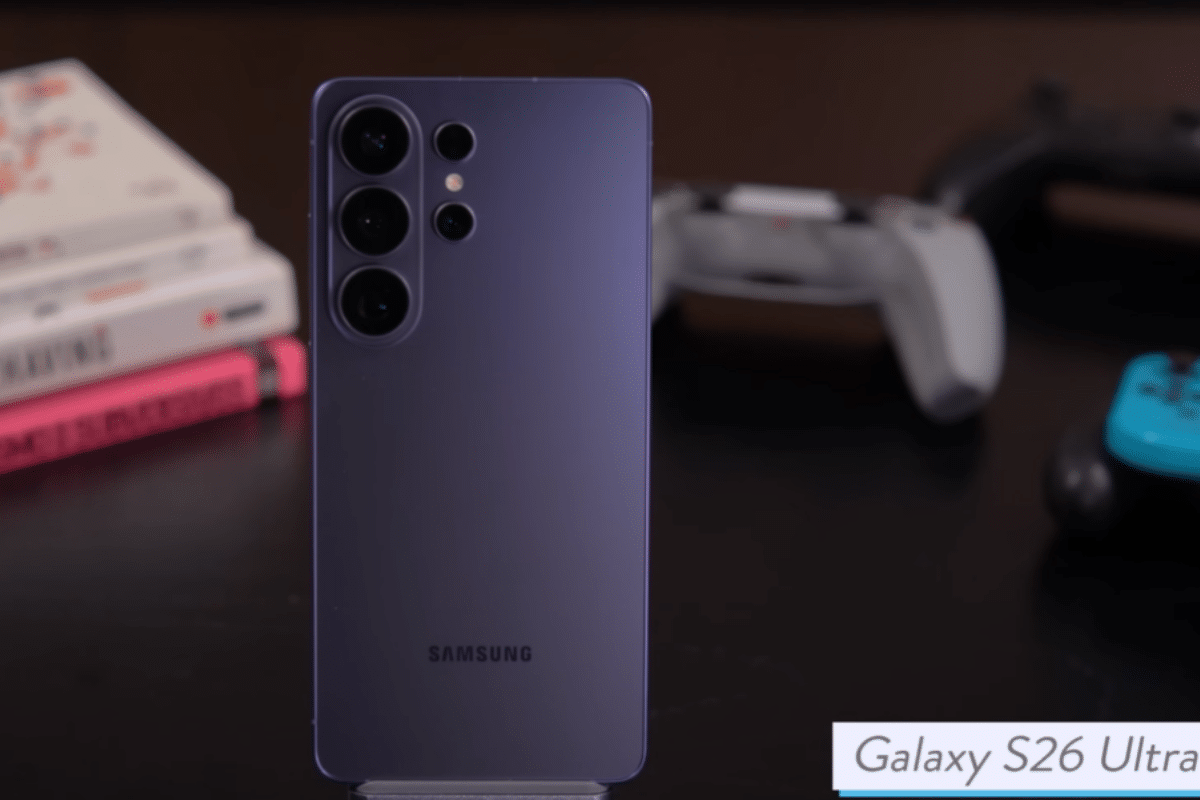 Galaxy S26 Ultra na cor roxa sobre mesa escura com livros e controles de videogame ao fundo