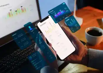 Smartphone exibindo gráficos e recursos inteligentes enquanto é usado em frente a um notebook, ilustrando o uso de inteligência artificial em tarefas cotidianas do celular.