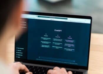 Pessoa utilizando laptop em uma mesa de madeira com a interface do ChatGPT aberta na tela, demonstrando o uso diário de inteligência artificial generativa.