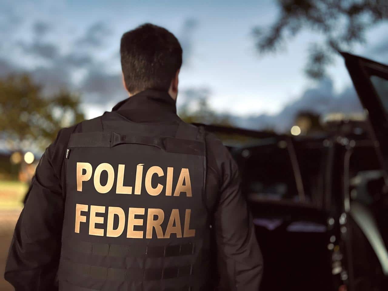 Agente da Polícia Federal ao lado de viatura durante operação institucional relacionada ao reforço do efetivo policial.