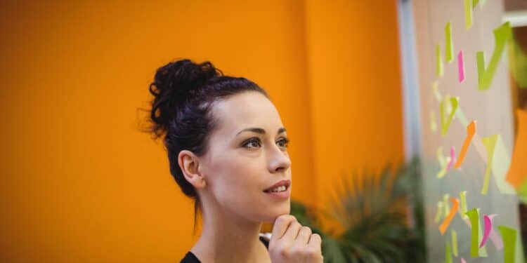 Mulher refletindo sobre notas adesivas em ambiente de trabalho, representando o signo de Peixes e suas características profissionais.