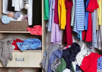 Interior de guarda-roupa com roupas penduradas e várias peças acumuladas e desorganizadas nas prateleiras e no chão.