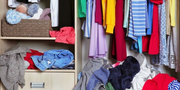 Interior de guarda-roupa com roupas penduradas e várias peças acumuladas e desorganizadas nas prateleiras e no chão.