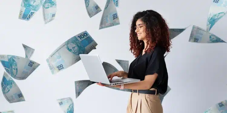Mulher sorrindo enquanto trabalha no notebook, com cédulas de 100 reais flutuando, representando o alto potencial de ganhos em carreiras sem diploma