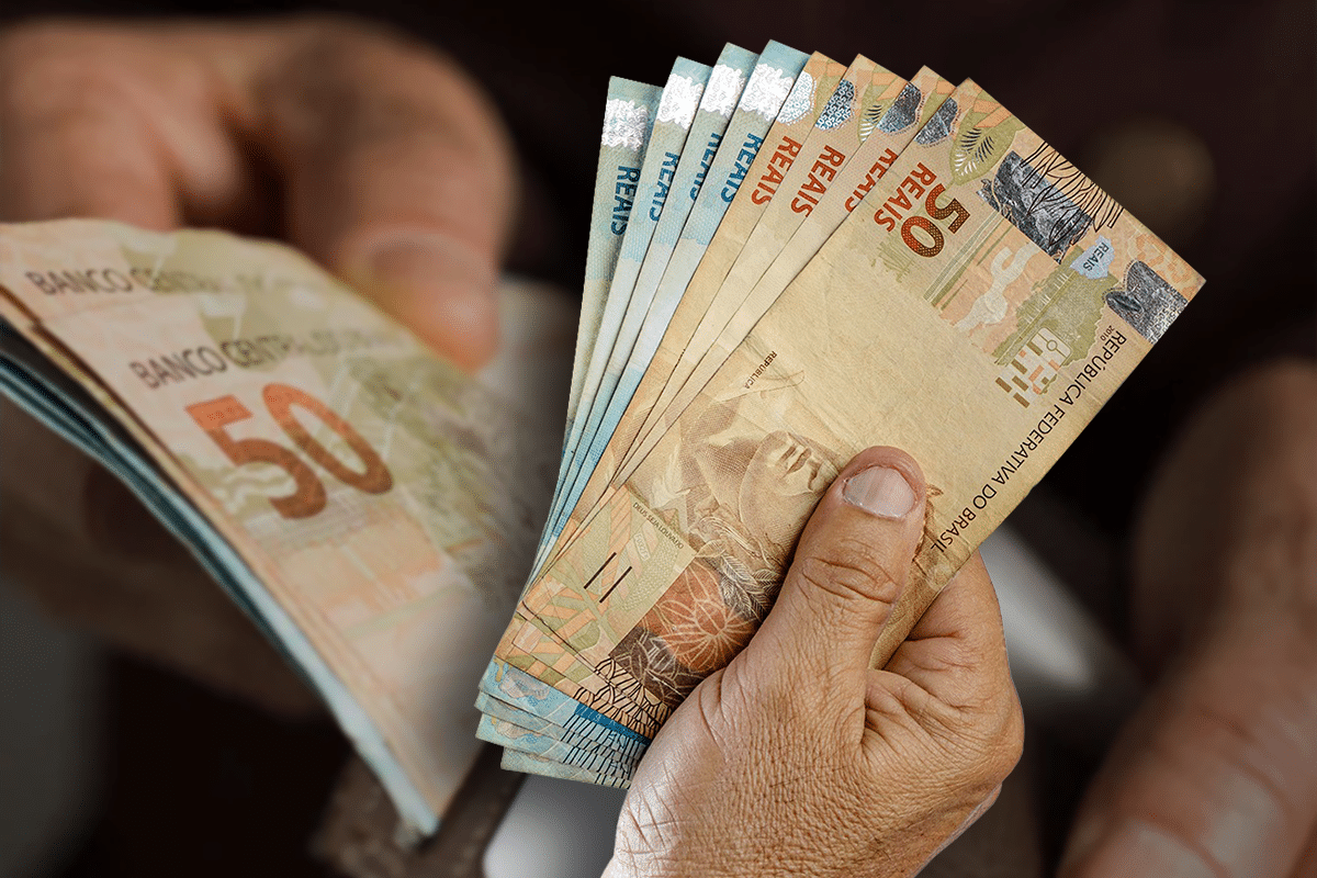 Mãos segurando várias notas de reais com destaque para cédulas de 50 reais