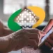 Mãos de pessoa idosa manuseando smartphone com o logotipo ampliado do INSS em verde e amarelo sobreposto à imagem, ilustrando o risco de fraude digital enfrentado por aposentados e pensionistas ao instalar aplicativos falsos que se passam pelo INSS