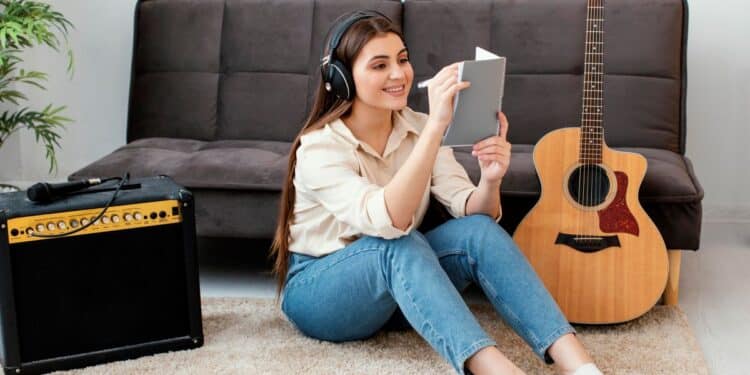 Jovem estudando inglês com música enquanto ouve fones de ouvido e faz anotações ao lado de um violão.