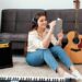 Jovem estudando inglês com música enquanto ouve fones de ouvido e faz anotações ao lado de um violão.