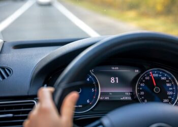 Motorista conduz veículo em rodovia com velocímetro indicando alta velocidade, ilustrando riscos associados ao aumento da velocidade no trânsito.