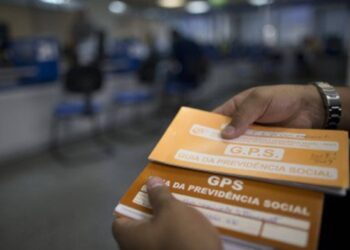 Mão segurando Guia da Previdência Social em agência do INSS