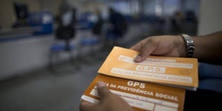 Mão segurando Guia da Previdência Social em agência do INSS