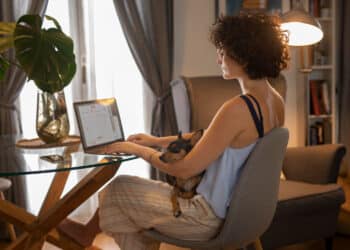 Mulher trabalhando em home office com notebook e cachorro no colo representando profissões remotas com salário acima de R$ 5 mil
