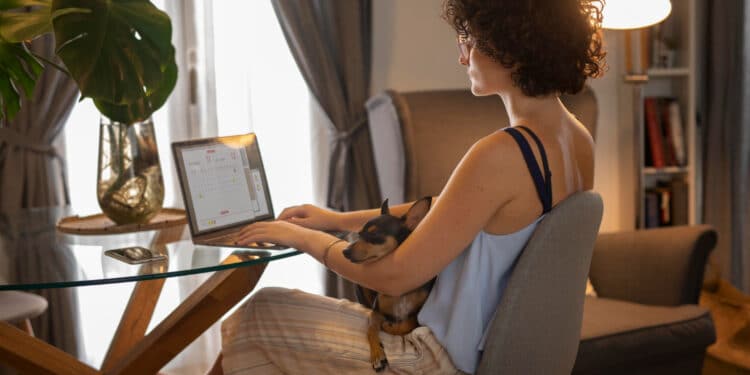 Mulher trabalhando em home office com notebook e cachorro no colo representando profissões remotas com salário acima de R$ 5 mil