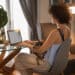 Mulher trabalhando em home office com notebook e cachorro no colo representando profissões remotas com salário acima de R$ 5 mil